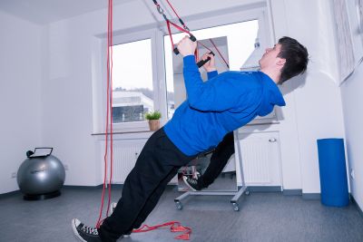 Physiotherapeut Tobias Henkel demonstriert eine Bewegung im Sling-Trainer des Bewegungsraum, Praxis f&uuml;r Physiotherapie